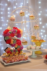 Party table, candies, homemade dessert, lovely details. Front view. Bokeh lights background. Letter S made by flowers decoration