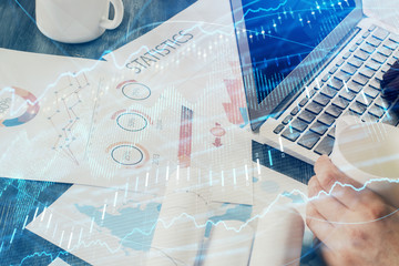 Double exposure of stock graph with businessman typing on computer in office on background. Concept of hard work.