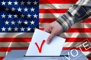 male hand of a voter lowers the ballot in the ballot box on the background of the usa national...