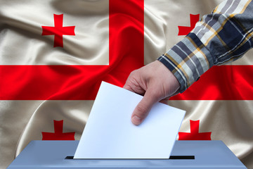male hand of a voter lowers the ballot in the ballot box against the background of the national...