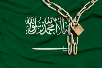 iron chain and lock on the silk national flag of kingdom of saudi arabia with beautiful folds, the concept of a ban on tourism, political repression, crime, violation of the rights and freedoms