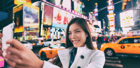 New York city tourist selfie Asian happy woman taking photo at night in Times Square, Manhattan,...