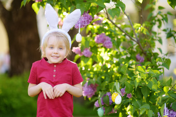 Pretty little boy wearing bunny ears hunting for easter eggs in spring park on Easter day.