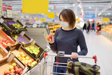 Young woman wearing disposable medical mask shopping in supermarket during coronavirus pneumonia...