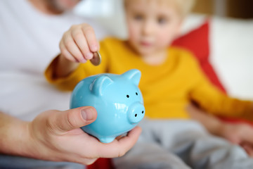 Father and child putting coin into piggy bank. Education of children in financial literacy