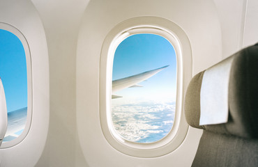 Inside of a plane window view of wing during flight of airplane interior with seat background.