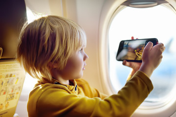 Little boy is taking a shot view of airfield from illuminator plane by smartphone. © Maria Sbytova