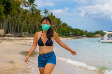 Fototapeta premium use of medical face mask in public places- young attractive Asian Korean woman enjoying beach holidays in bikini and protective facial mask in prevention vs virus infection