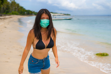 use of medical face mask in public places- young attractive Asian Korean woman enjoying beach holidays in bikini and protective facial mask in prevention vs virus infection