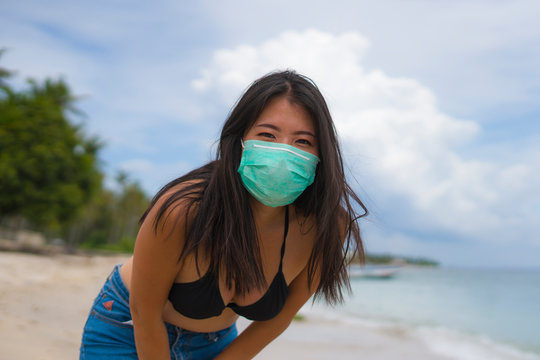 Use Of Medical Face Mask In Public Places- Young Attractive Asian Korean Woman Enjoying Beach Holidays In Bikini And Protective Facial Mask In Prevention Vs Virus Infection