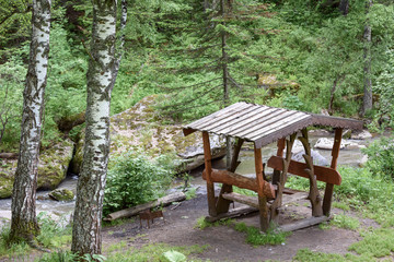 Secluded gazebo with a wooden table and seats inside for relaxation and entertainment in the forest.