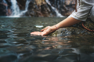 Close hand of a woman in white clothes by a waterfall