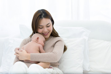 Beautiful mom supports and tenderly cuddles the newborn baby gently while the infant is sleeping on the chest. Asian mother looking at the baby with love and showing protection.