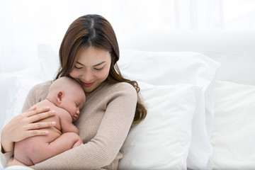 Beautiful mom supports and tenderly cuddles the newborn baby gently while the infant is sleeping on the chest. Asian mother looking at the baby with love and showing protection.