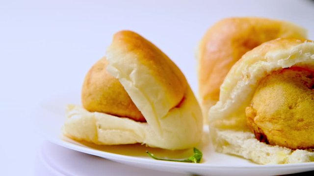 Vada pav on white plate with green mirchi in closeup, rotating against white background