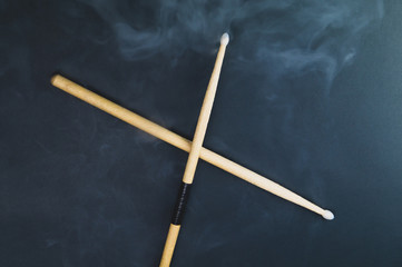 A pair of wooden drumsticks in the smoke on color background