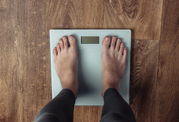 Woman with bare feet is weighed on the scales on the floor. Top view. Fitness concept