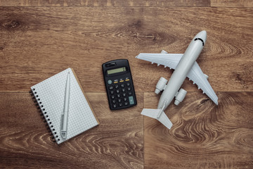 Travel concept. Calculation of the cost of vacation. Plane figurine, calculator and notebook on wooden floor. Top view. Flat lay