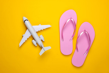 Travel flat lay composition. Plane figurine, flip flops on a yellow background. Beach vacation. Top view