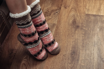 Female legs in warm cozy socks on a wooden floor in the room.