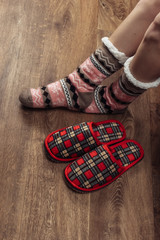 Female legs in warm cozy socks with  slippers on wooden floor in the room.