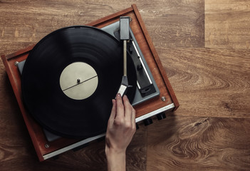 Female hands set up a retro vinyl record player on a wooden floor. Music lover, 70s, nostalgia, top...