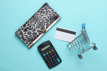 Stylish wallet, shopping trolley with bank card and calculator on blue background. Shopping concept. Top view. Flat lay