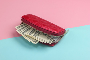 Red wallet with hundred dollar bills on a blue-pink pastel background.