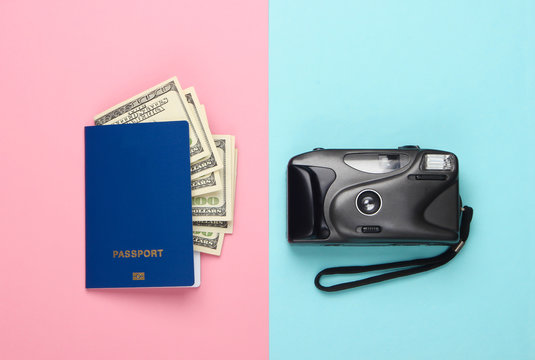 Passport with dollar bills and a camera on a blue-pink pastel background. Flat lay travel composition. Top view