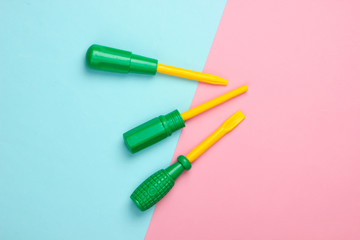 Set of plastic toy screwdrivers on pink blue pastel background