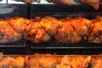 Whole chickens being roasted in a rotisserie oven behind clear perspex covers