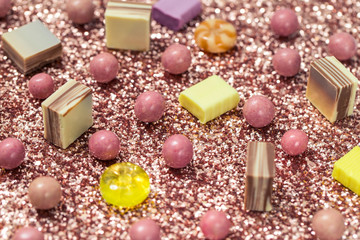 Sweet candies on a sparkling background. Caramel toffee, milk chocolate, round yellow lollipops with pink and gold sequins