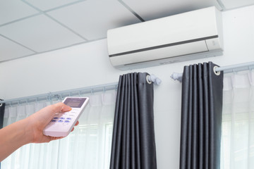 Hand pressing remote control air conditioner in room.