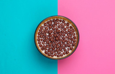 Chocolate cereal balls with milk in bowl on pink blue background. Concept for a healthy diet. Top view