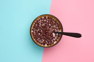 Chocolate cereal balls with milk and spoon in bowl on pink blue pastel background. Concept for a...