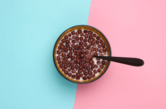 Chocolate Cereal Balls With Milk And Spoon In Bowl On Pink Blue Pastel Background. Concept For A Healthy Diet. Top View