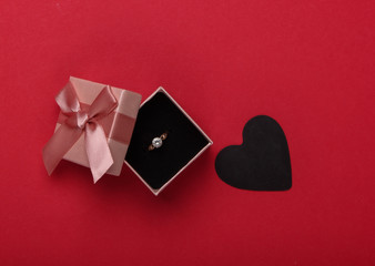 Romantic concept. Golden ring with diamond in box, black hearts on red background. Marriage proposal, gift for Valentine's Day, Black Friday. Top view
