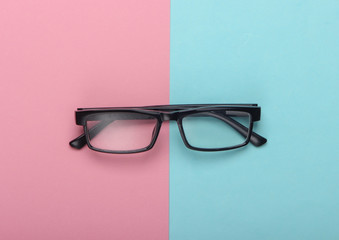 Classic eyeglasses on pink blue pastel background. Top view. Minimalism