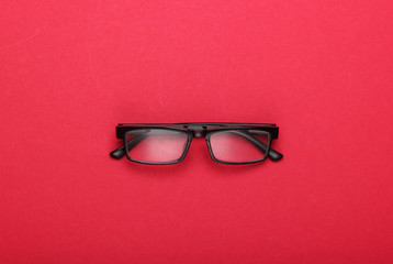 Classic eyeglasses on red background. Top view.