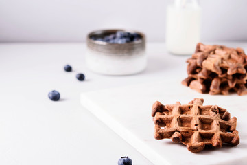 Homemade Chocolate waffles, milk and blueberries on white marble tray. Breakfast. Selective focus