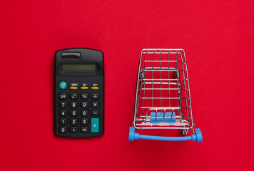 Shopping trolley with calculator on red background. Economic calculation of shopping, purchase...