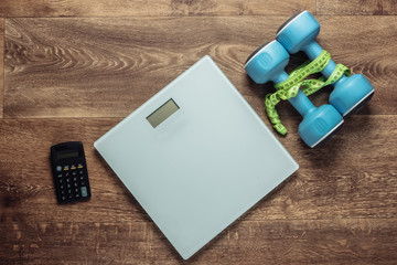 The concept of weight loss, fitness. Calorie Counting. Floor heights, calculator and dumbbells, measuring tape on wooden floor. Top view