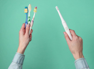 Woman's hands holding a new electro toothbrush and old used toothbrushes on a blue background