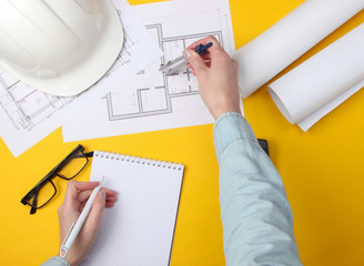 Engineering workspace. Female hands make calculations and measurements on a yellow background. Top view