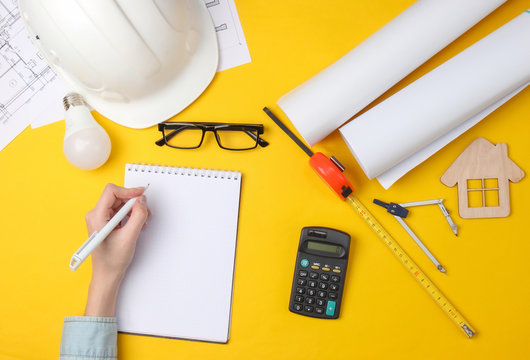 Female hand writes in a notebook. Engineer workspace. Top view. Analysis of the cost of building a house