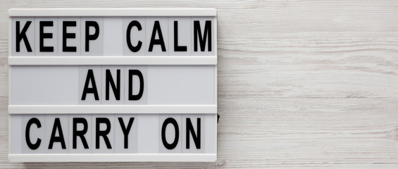 'Keep calm and carry on' words on a lightbox on a white wooden background, top view. Overhead, from...
