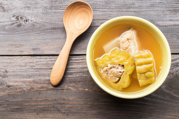 Bitter gourd soup with pork ribs in bowl on wood table.