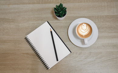 top view of notebook next to a pen and cup of coffee on wooden table with copy space.