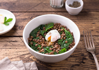 Boiled lentils with spinach, herbs, spices and poached egg in ceramic bowls on a wooden background. Simple healthy homemade food	