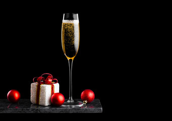 Elegant glass of yellow champagne with bubbles with christmas new year gift box and toys on marble board on black background Space  for text